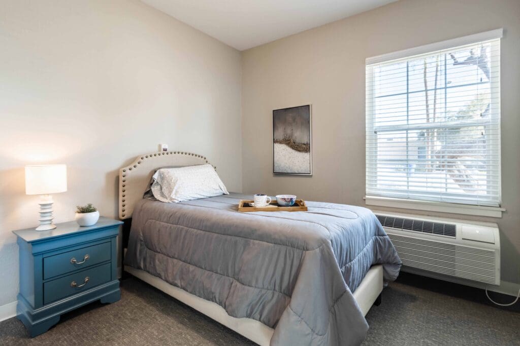 Interior image of a resident's bedroom, decorated with comfortable furniture. A tray on the bed holds a mug and a bowl.