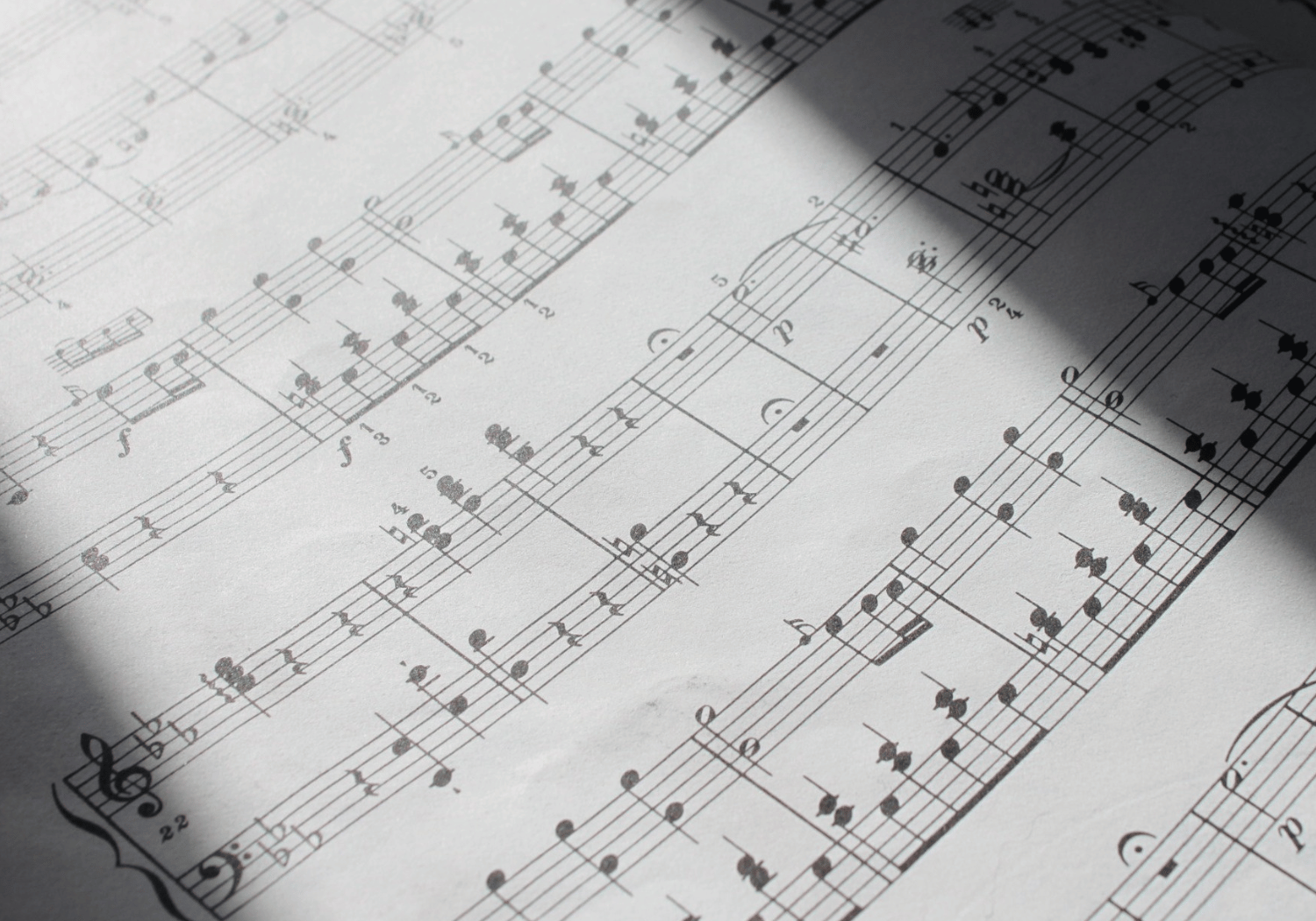 Close-up of classical sheet music with multiple staves and notes, with diagonal shadows across the page.